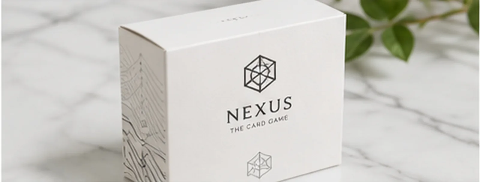 A white card game box on marble, the title blind embossed and a fine map pattern running down the side panel