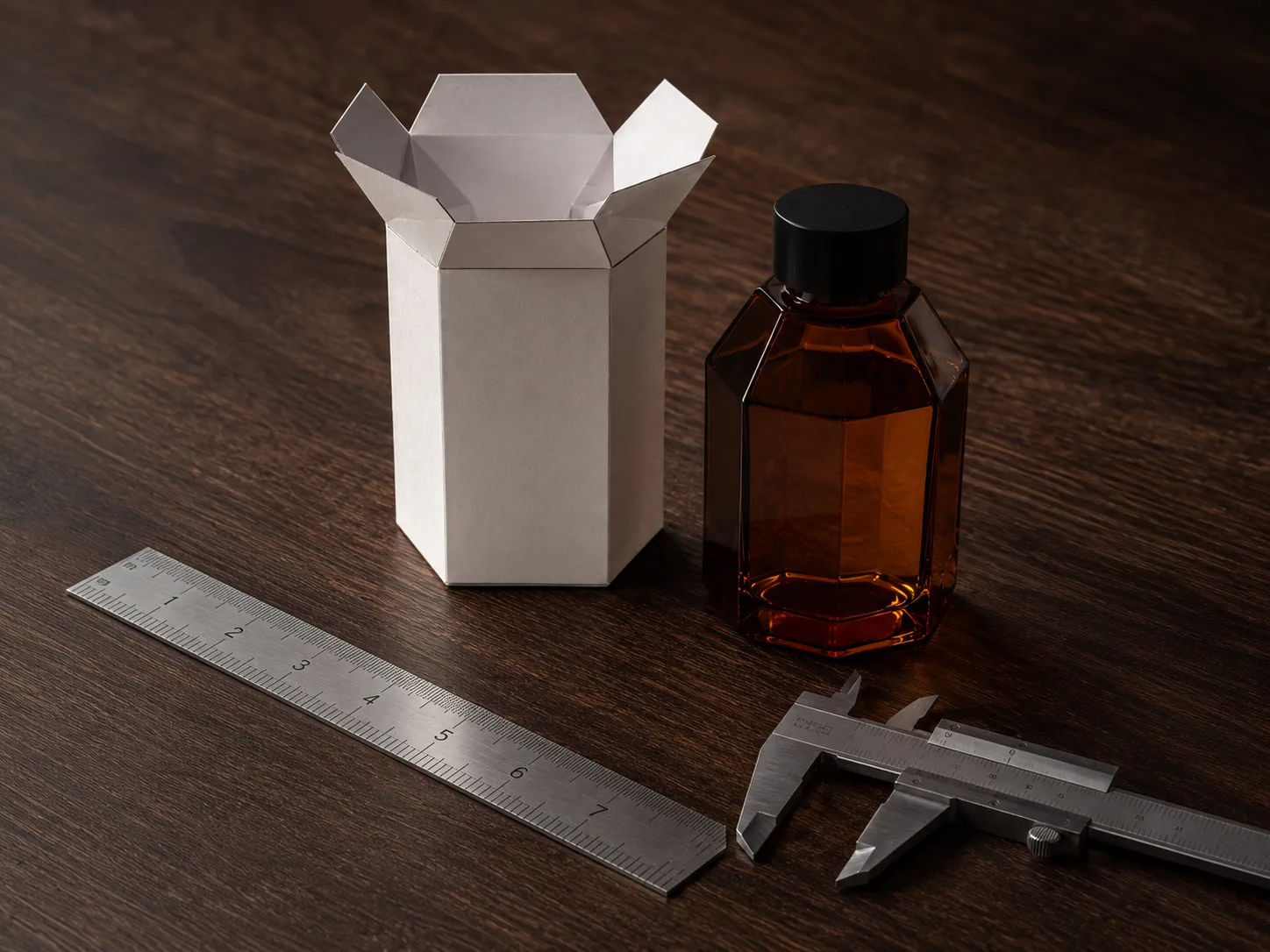 A faceted amber bottle and the white hexagonal carton drawn around it standing on a dark bench beside a steel rule and a vernier caliper, nothing else in frame.