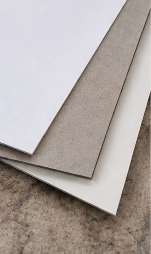 Three unprinted duplex board sheets fanned on a speckled stone surface, a white print face on top, a gray back in the middle and a white back underneath