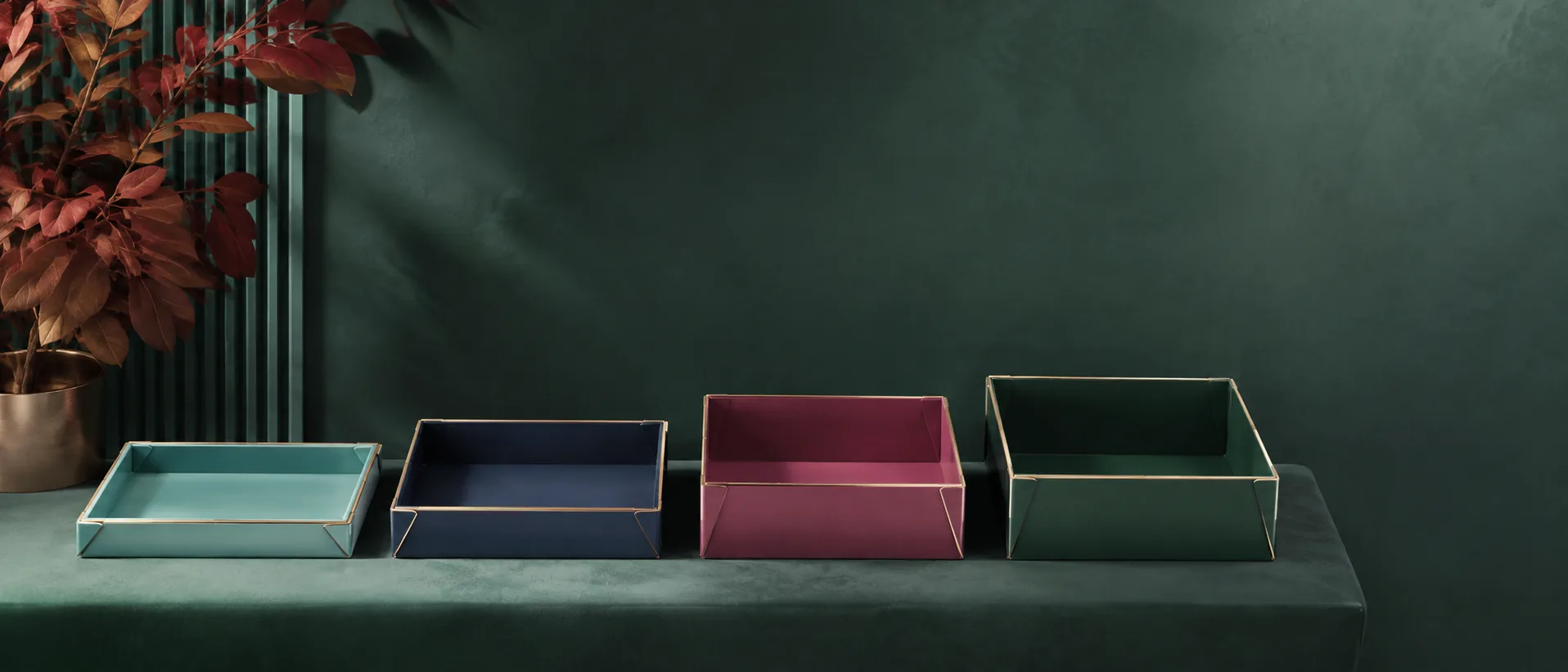 Four empty four corner trays in a row on a bench in graded depths, shallow to deep, the glued corners catching the light.