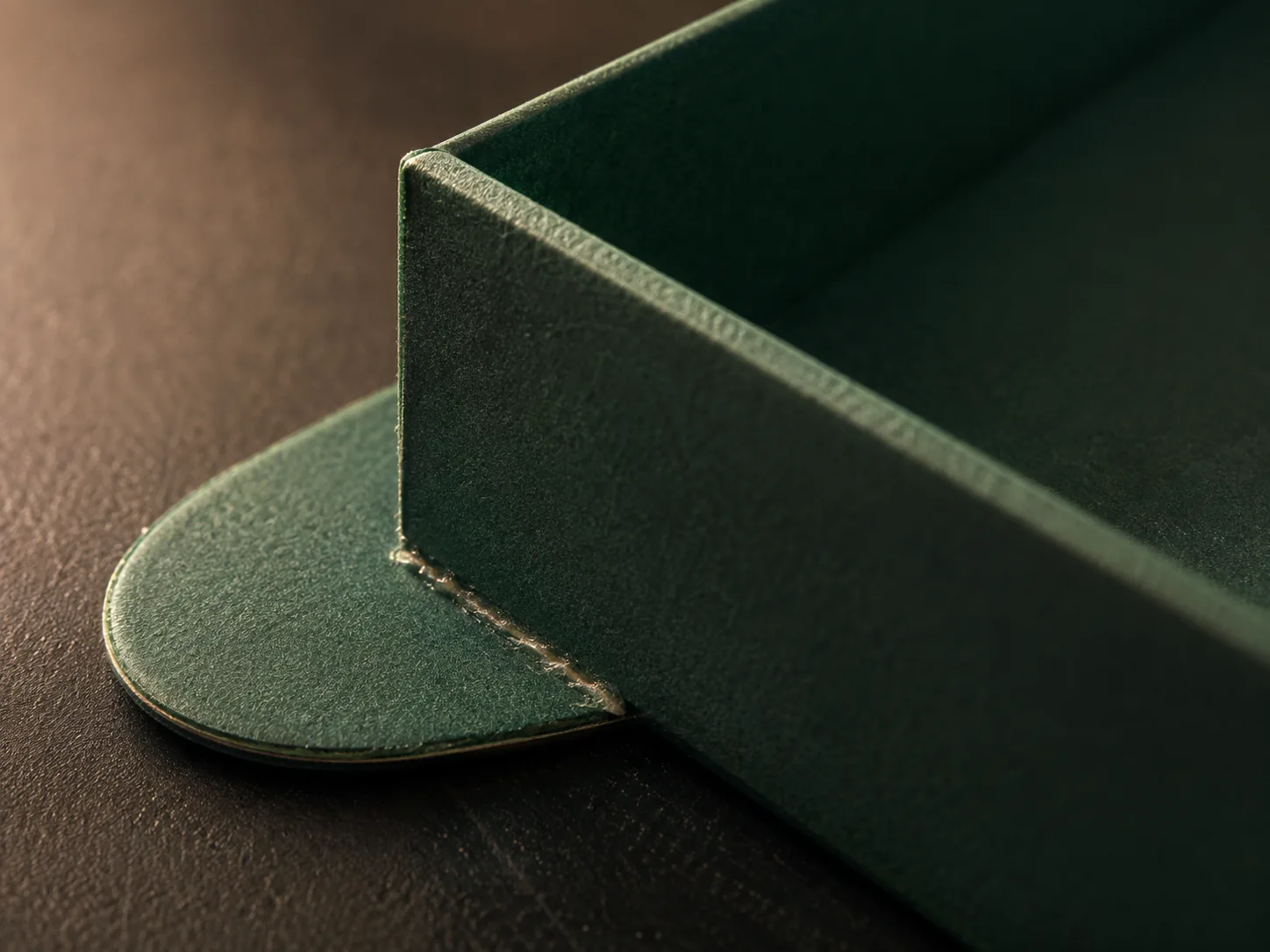 A macro of one glued corner of a green tray, the tapered ear lying flat behind the end wall with the glue line catching raking light.