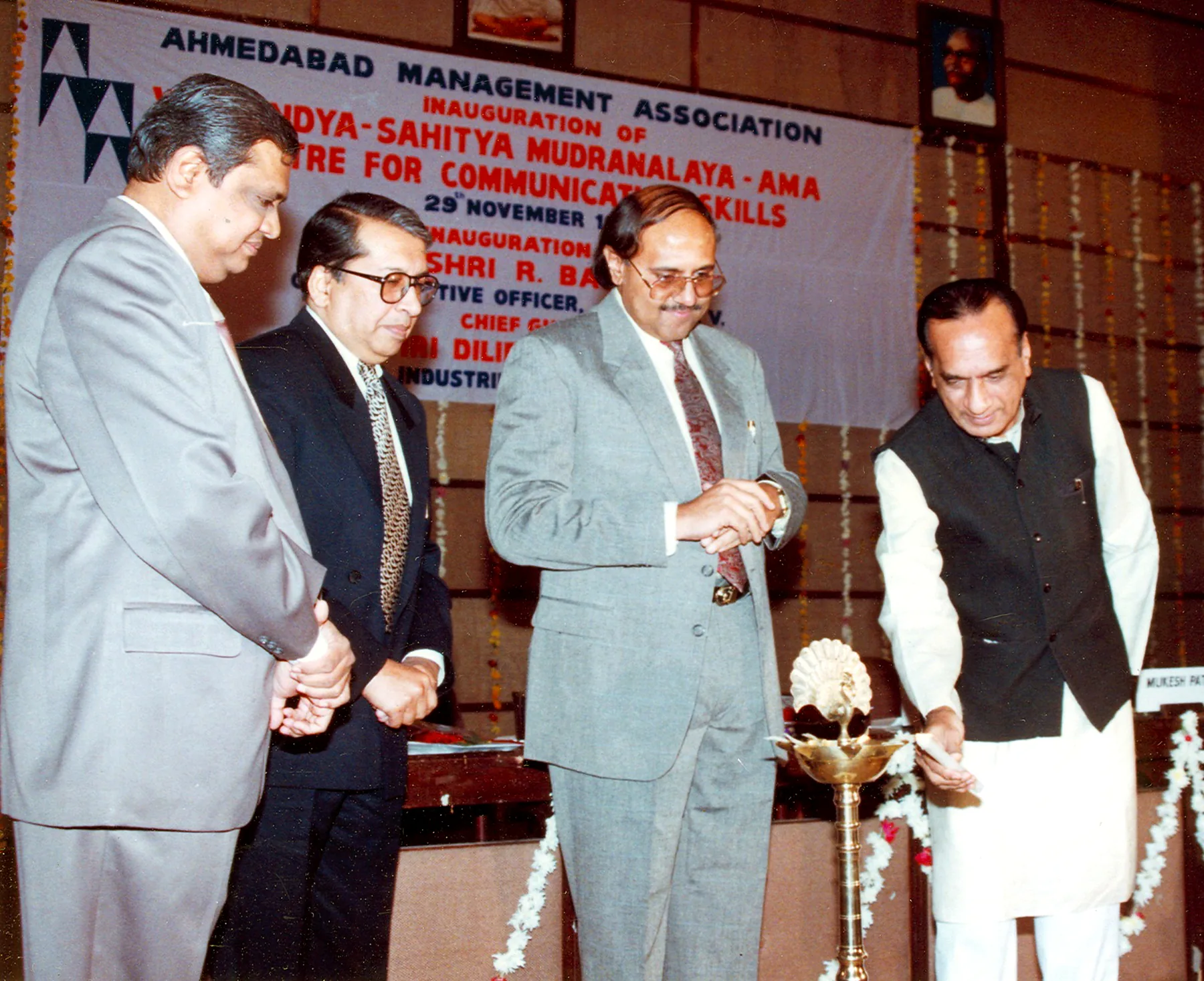 Four men in suits at a lamp lighting under an Ahmedabad Management Association banner announcing the inauguration of the Sahitya Mudranalaya AMA Centre for Communication Skills on 29 November.
