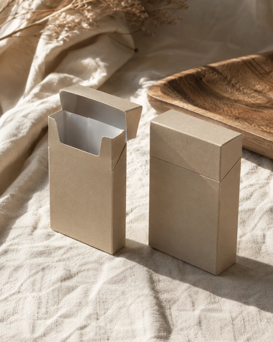 Two kraft hinge lid packs on linen in low sun, one open with the lid standing back and the shoulder showing, one closed beside it.