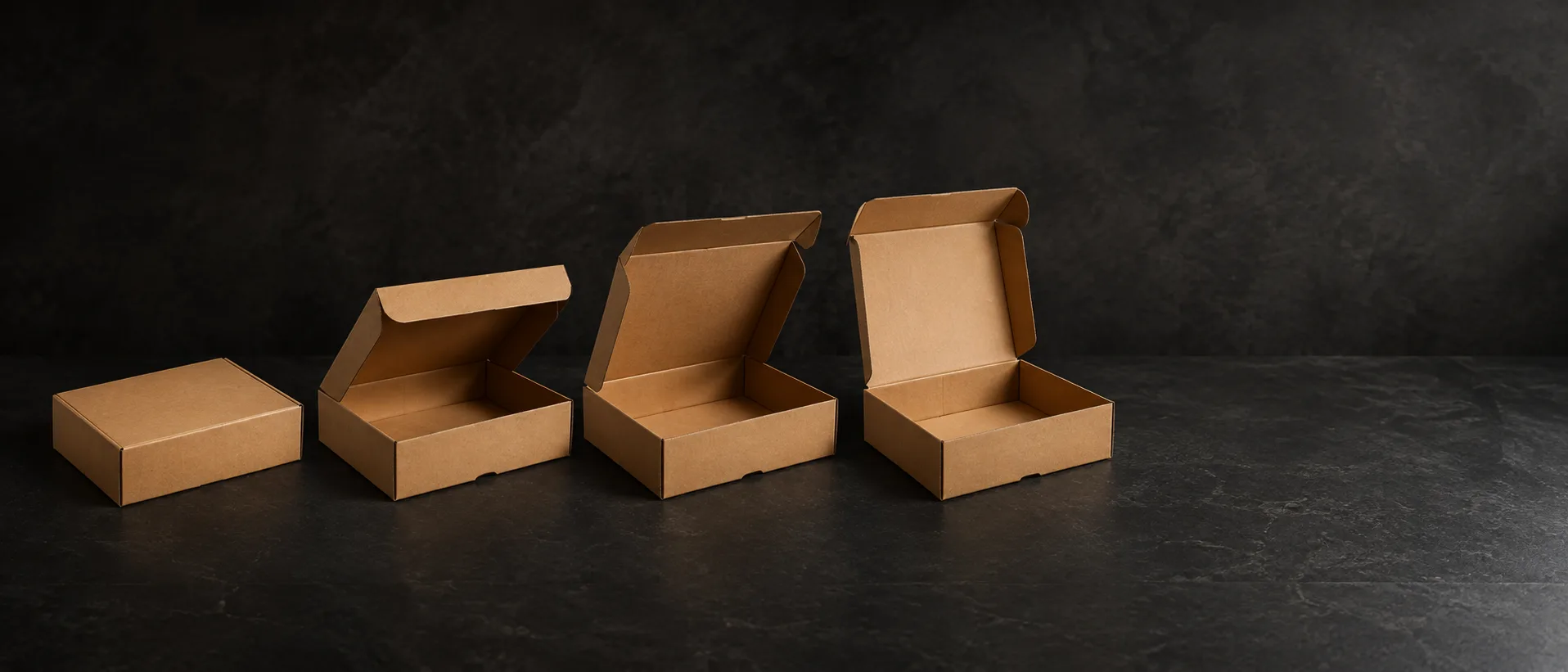 One kraft hinge lid box photographed in four positions across a dark stone bench, shut at the left and fully open at the right.