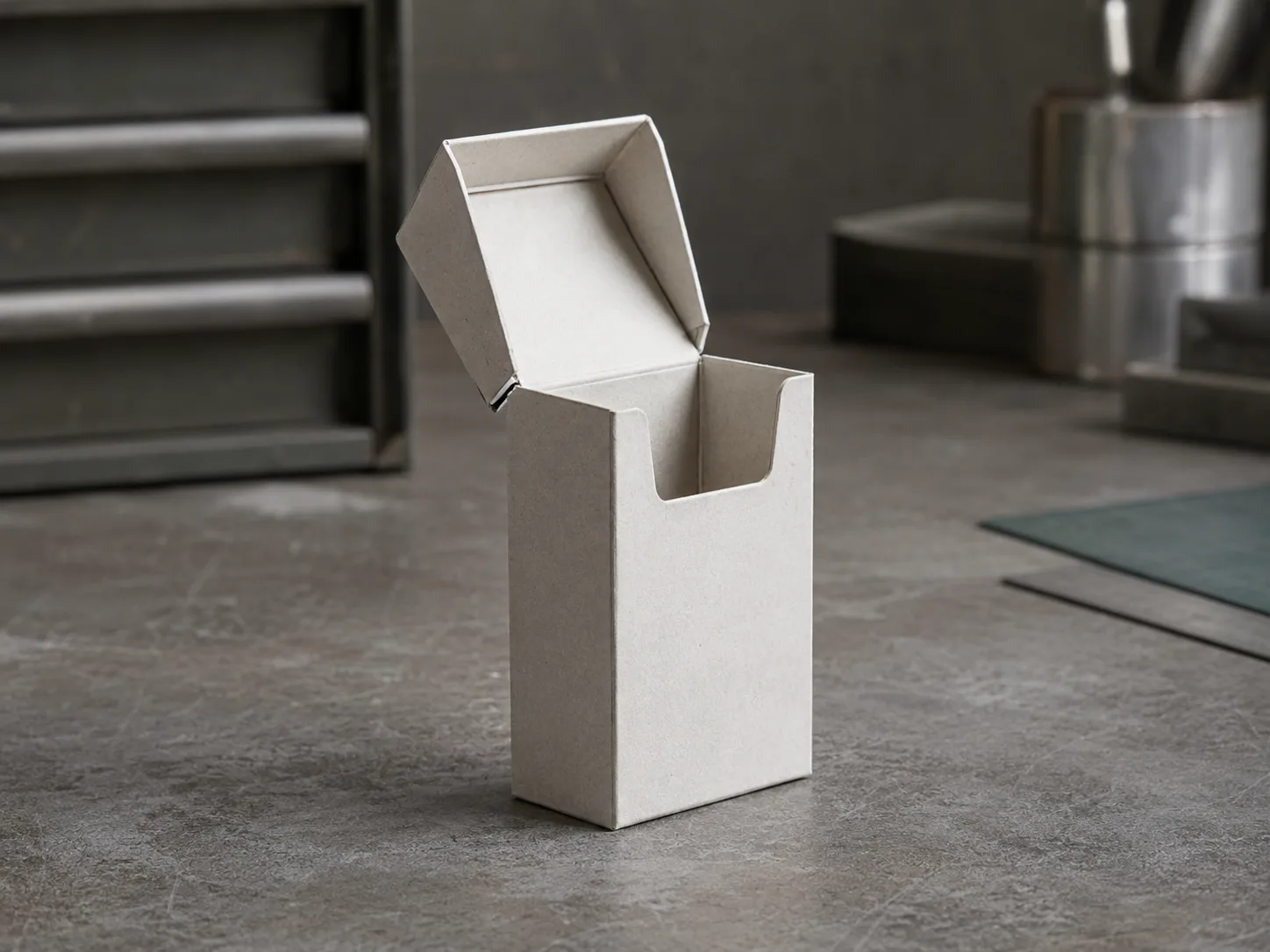 A gray board hinge lid carton open on a workbench, shot from the side so the lid chain creases and the natural rest angle of the lid both read.