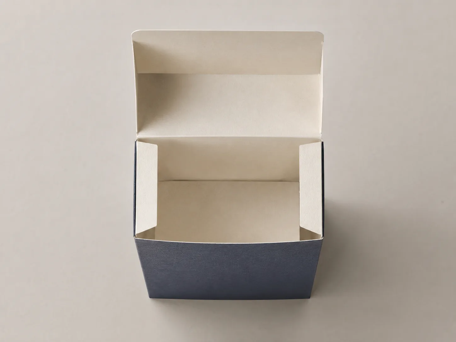 Looking straight down into an open navy hinge lid carton, both cream shoulder flaps folded in across the top of the side walls and the lid standing back behind.