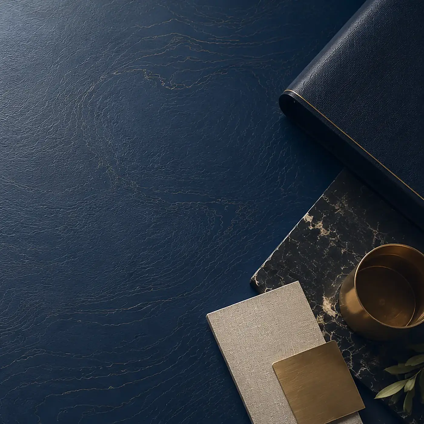 A navy vinyl table mat seen from above, a second mat rolled beside it with a brass cup, a marble tray and linen and brass swatches