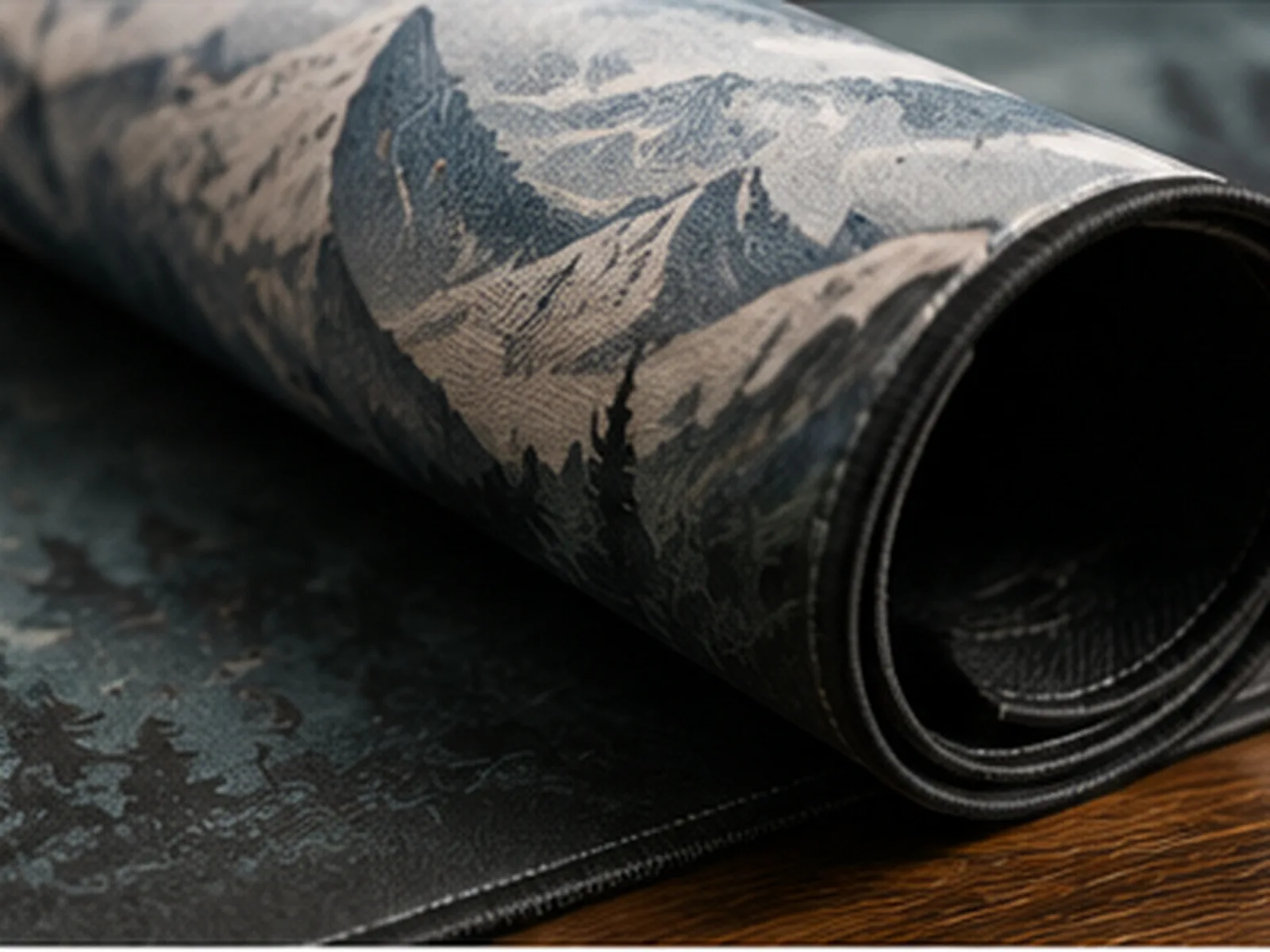 A mountain-print mat rolled for storage beside a flat one, the stitched edge visible along the roll