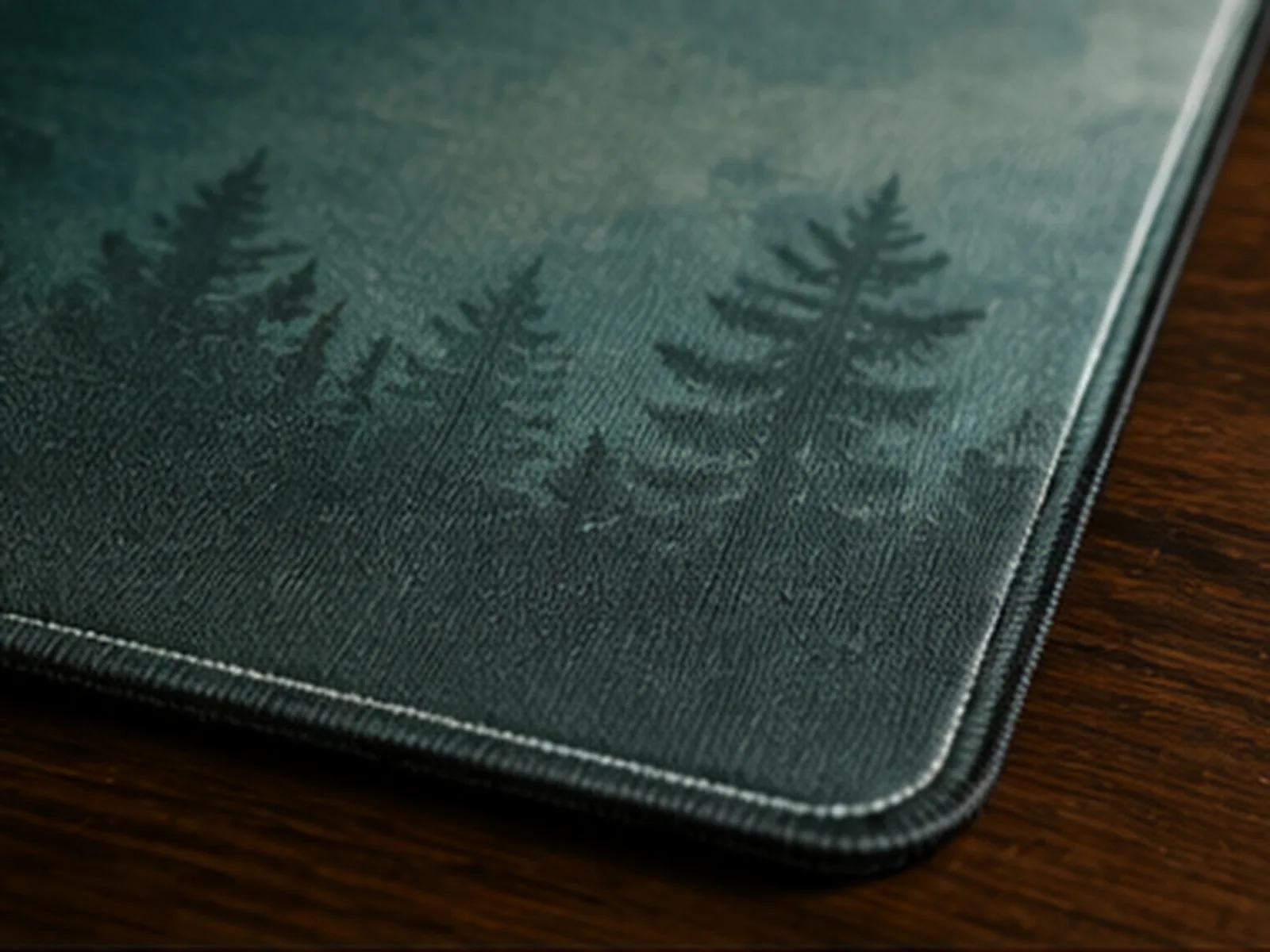 The corner of a teal forest-print mat on dark wood, the stitched edge running along both sides