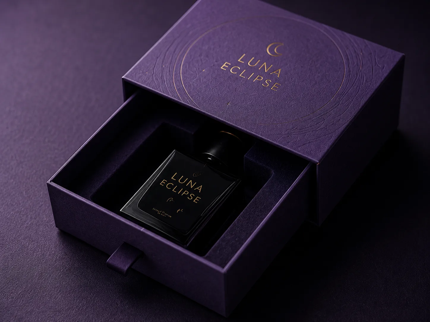 A purple soft touch drawer box under raking light, its lid carrying a blind embossed orbit and a gold foiled wordmark