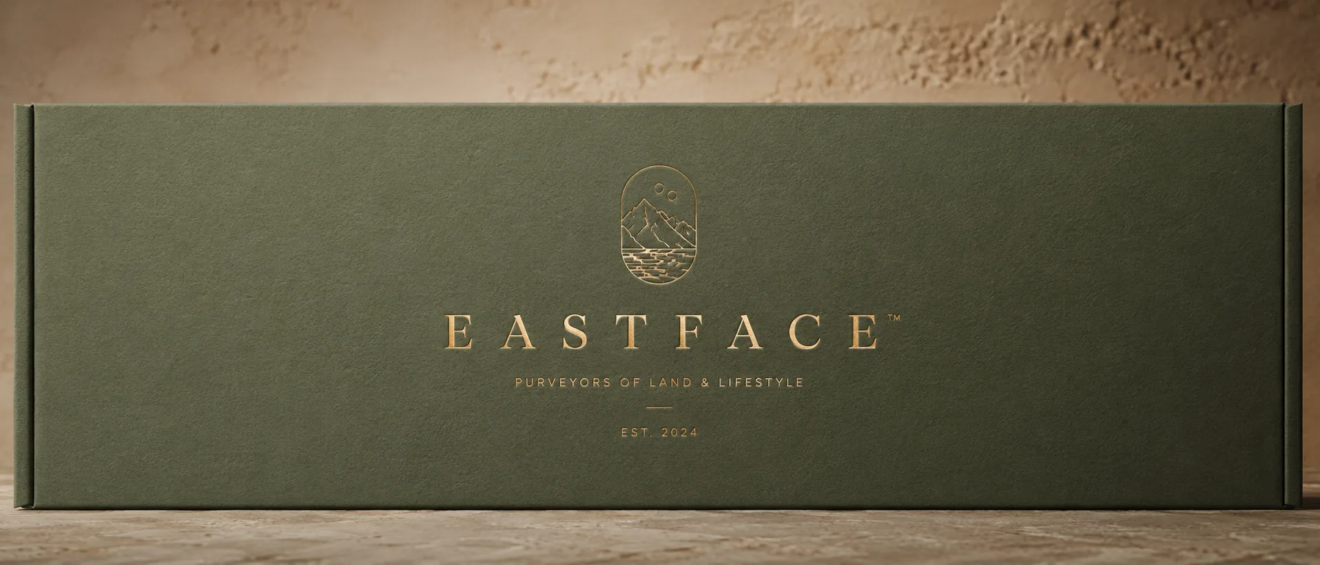 A deep green uncoated face panel under raking light, a gold foil wordmark and crest standing off the board