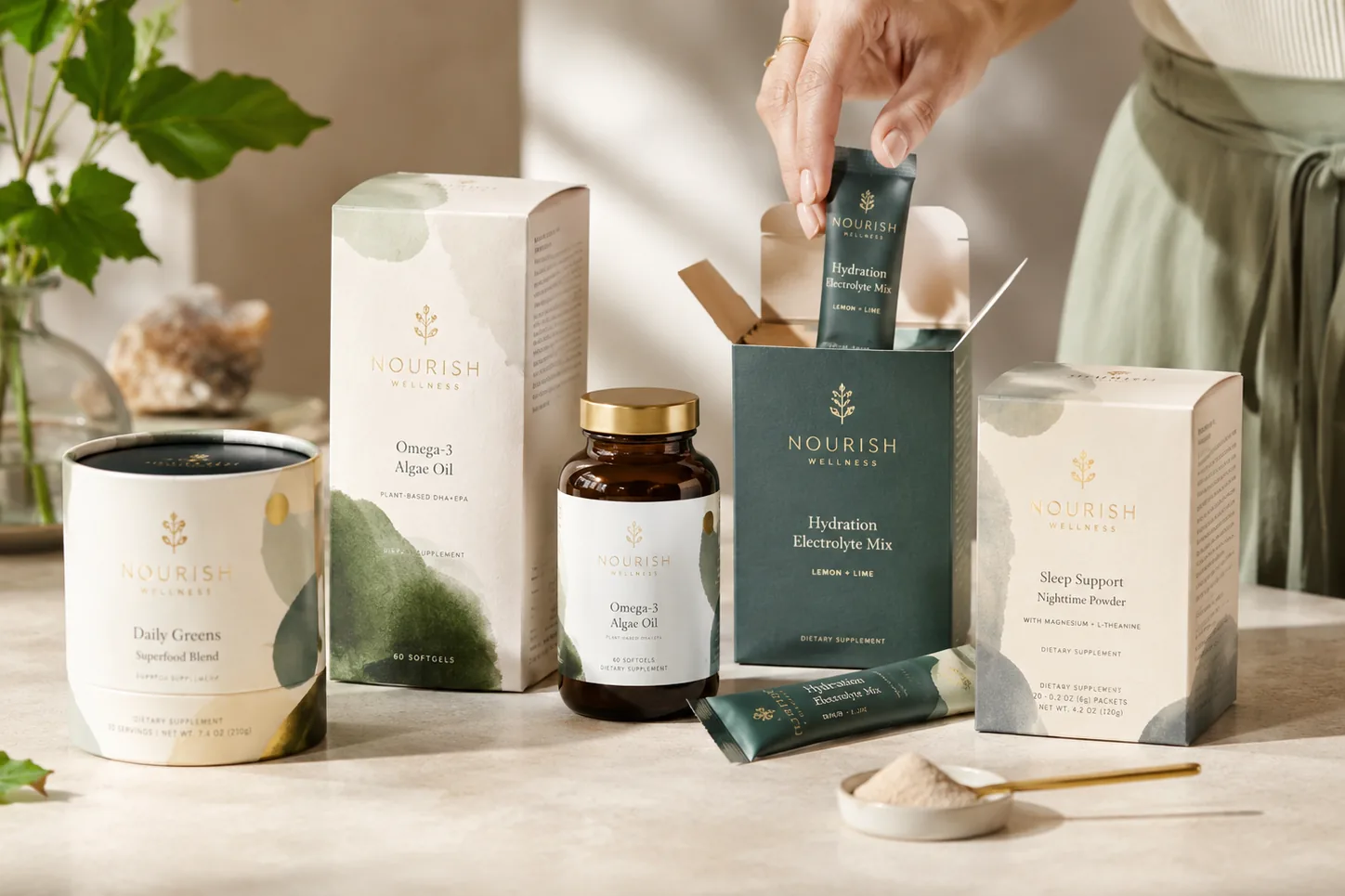 A supplement range on a warm neutral counter: a powder canister, an omega carton, a bottle, a sachet dispenser and a sleep support carton, a hand drawing one stick pack out
