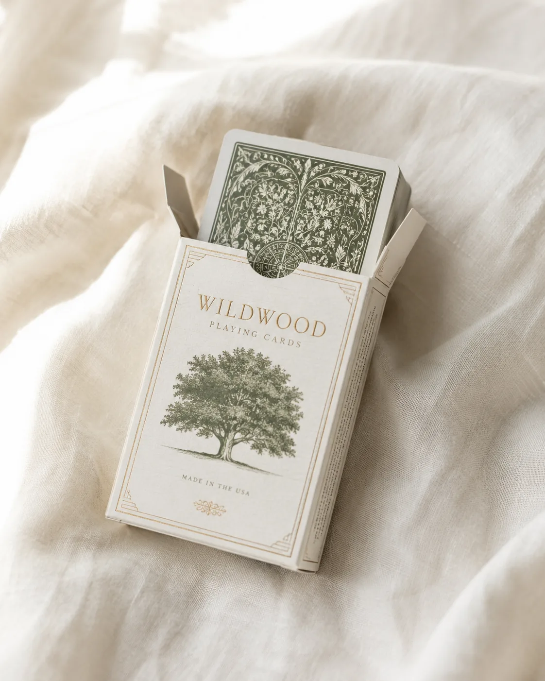 An open tuck box on linen with a printed card deck standing half out of it, the tuck flap folded back and both dust flaps up